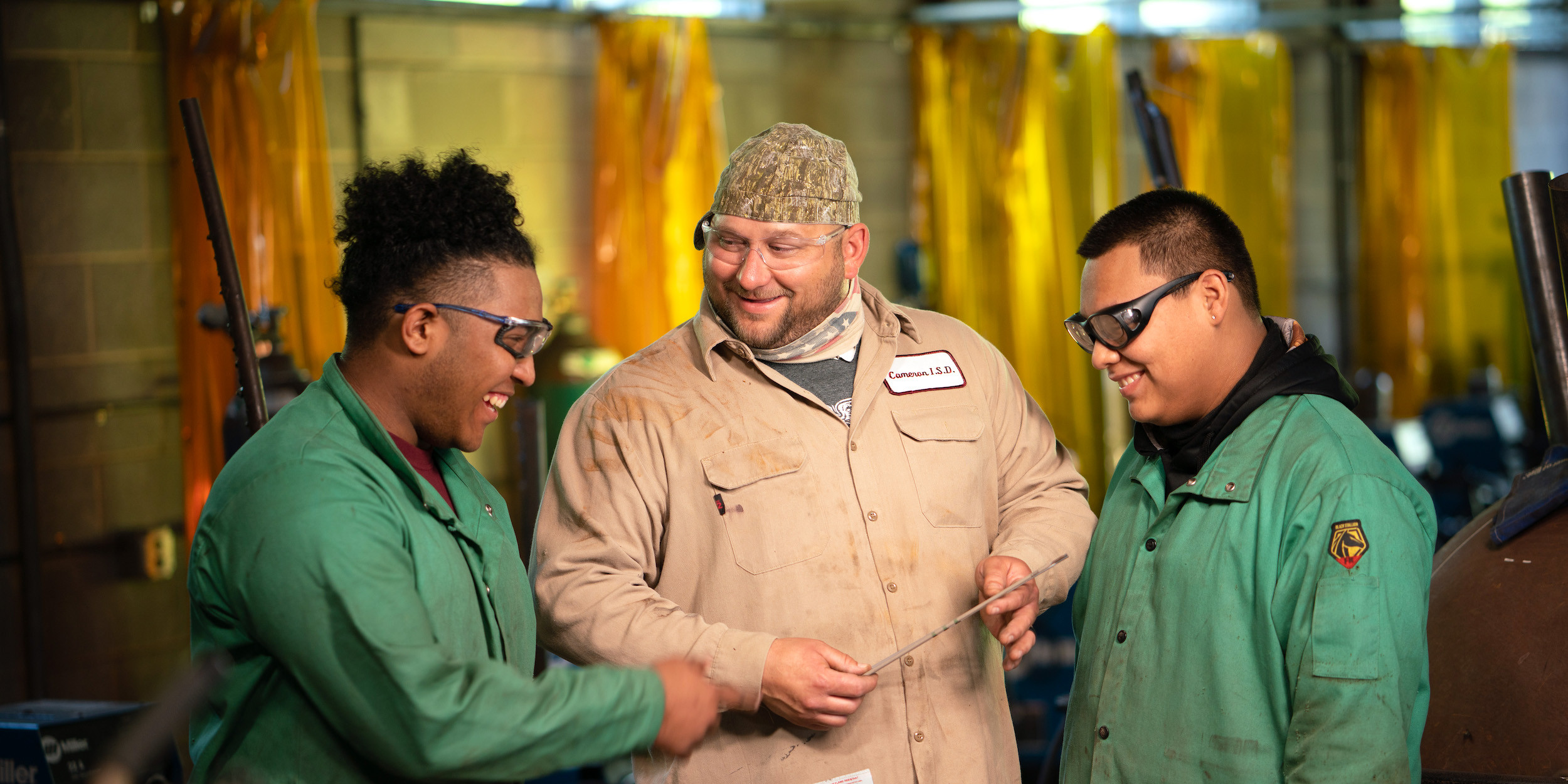A teacher showing two students a piece of welding equipment